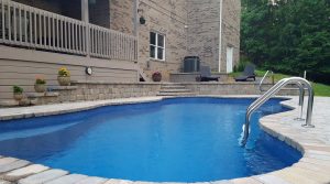 Large Fiberglass Swimming Pool With Tile Pavers on Hilly Yard
