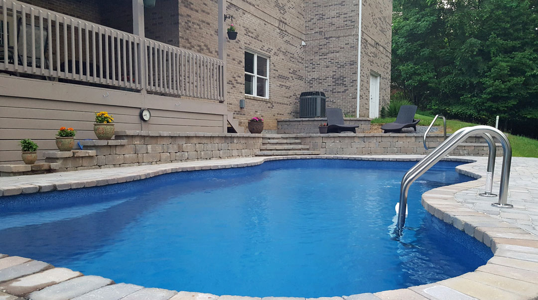 Large Fiberglass Swimming Pool With Tile Pavers on Hilly Yard