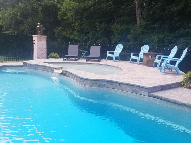 Swimming pool tanning ledge feature with firepit and waterfall