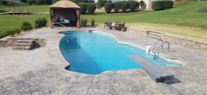 Fiberglass pool with diving board on terraced hill with pool cabana