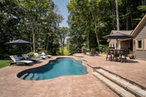 This inground fiberglass lagoon pool with integrated stair entry radiates a refreshing calm alongside the forest edge