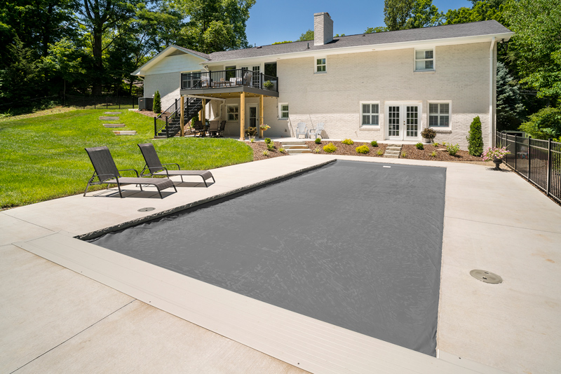 Simple elegant backyard pool with safety cover in place matches nicely with white house nearby