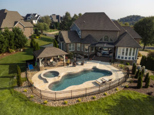 Backyard pool complex with shaded lounge area, pool cabana with outdoor kitchen, lagoon shaped fiberglass pool, and soaker tub with waterfall