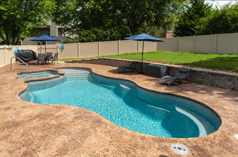 Small fiberglass lagoon shape inground pool and hot tub combo in a backyard with privacy fence