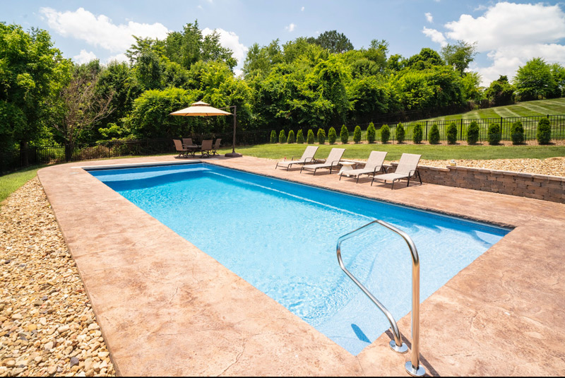 Large rectangular fiberglass inground pool with a retractable cover and tanning ledge, set by the edge of the woods in Kingsport, TN