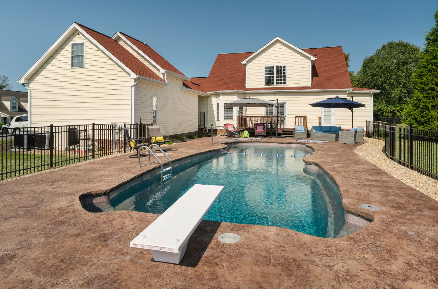 Backyard pool with deep end and diving board in a compact installation with metal safety fence