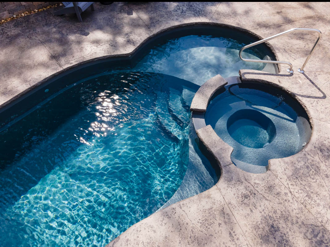 Detail overhead photo of one end of lagoon pool with integrated tanning ledge, jetted tub, and waterfall