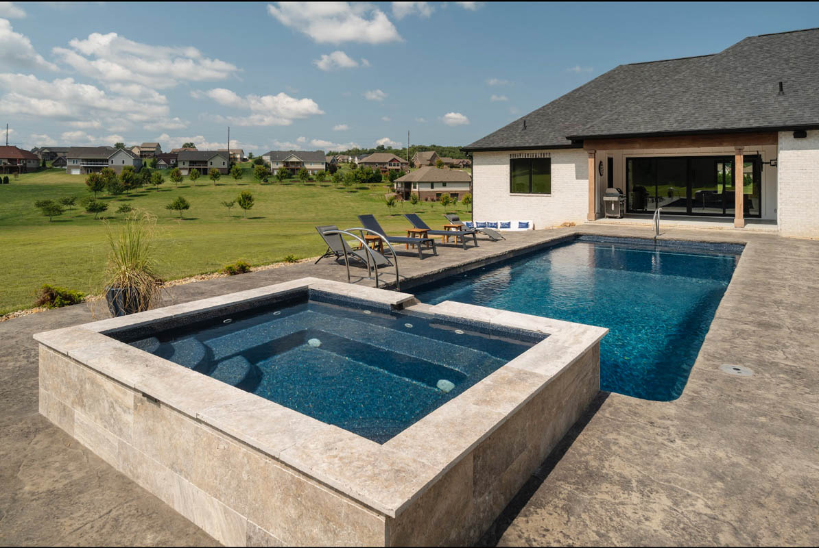 Jetted tub cascades into long rectangular lap pool with rolling hills and home in the background