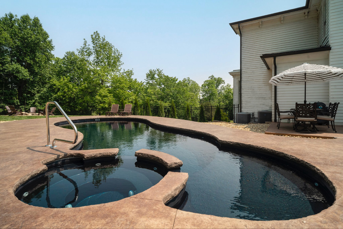 Lagoon pool with overflow spa by firepit behind a historic farm house
