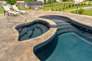 Inground swimming pool detail with dark blue fiberglass gelcoat, spa, and elegant security fencing