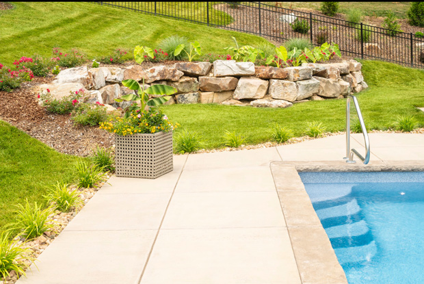 A dry stacked boulder retaining wall creates a level grassy nook poolside in this hilly backyard