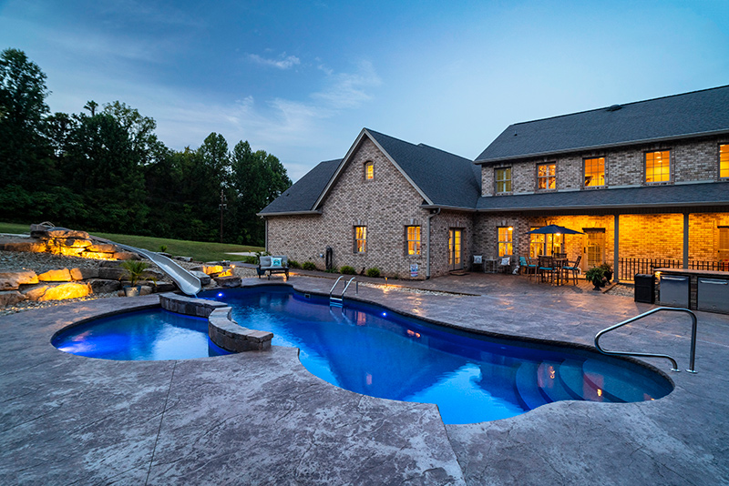 The backyard pool area illuminated at night with subdued landscaping lighting and integrated pool lighting