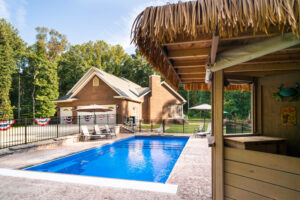 Backyard pool fenced in with patriotic bunting on fence and Margaritaville style tiki bar hut