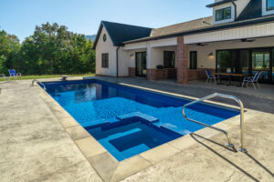 Large rectangular inground pool just steps outside covered patio with outdoor kitchen on back of house