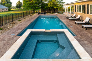 Inground lap pool with deep end and a jetted spa at the end with an overflow waterfall alongside a brick ranch house