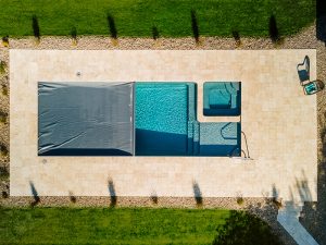 Overhead drone photography of rectangular inground swimming pool with safety cover partially retracted