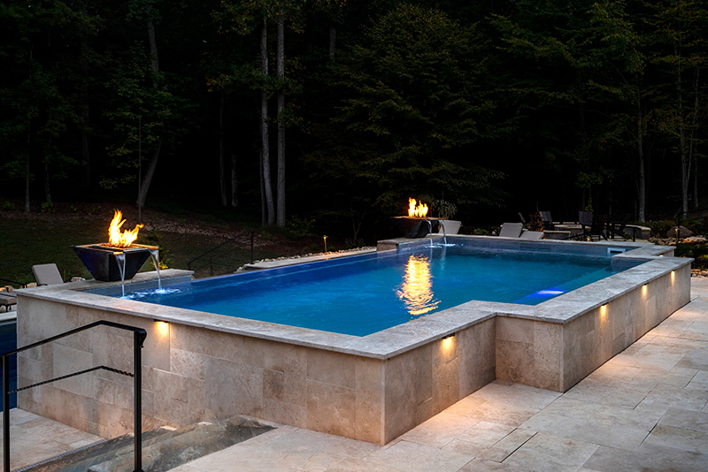 The upper pool at night with lit fire bowls and elegant walkway lighting