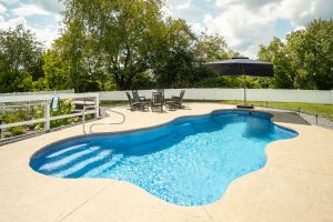 Fiberglass pool looking inviting on a warm summer day in fenced backyard alongside a beautiful large willow tree