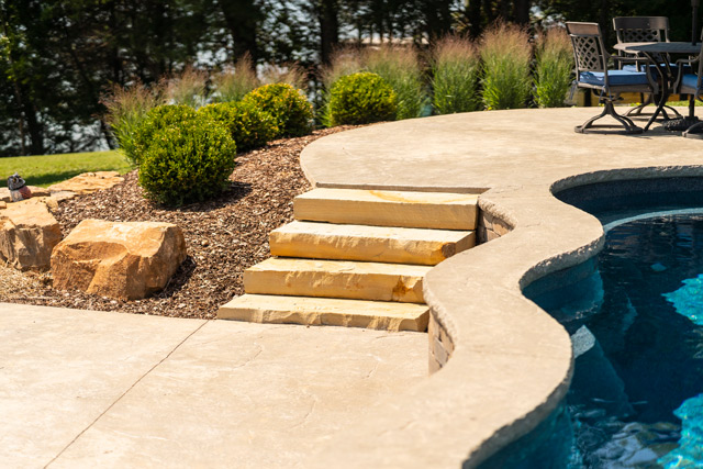 Closeup photo of deep blue pool finish alongside buff earthy tones of stamped colored concrete and natural stone landscaping material