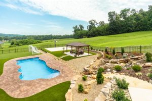 Amazing backyard remodel with small soccer and basketball goal areas, terraced landscaping with copious us of natural boulders, a waterfall, and seating area under a pergola